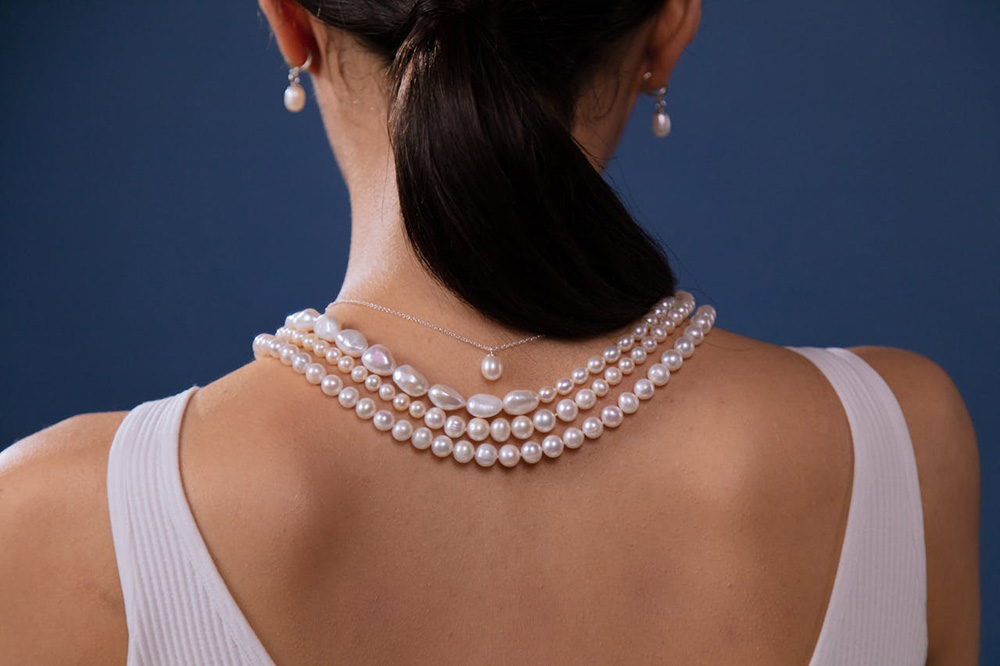 Jaxon's Jewelry modeled on a woman with dark hair that is facing away while the pearl necklaces are drapoed around her neck for display.